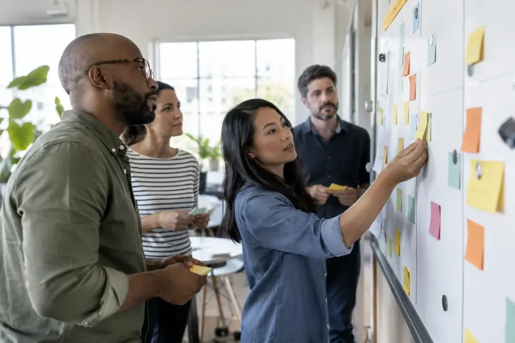 A small team moving unlettered task cards across a planning board during a practical meeting.