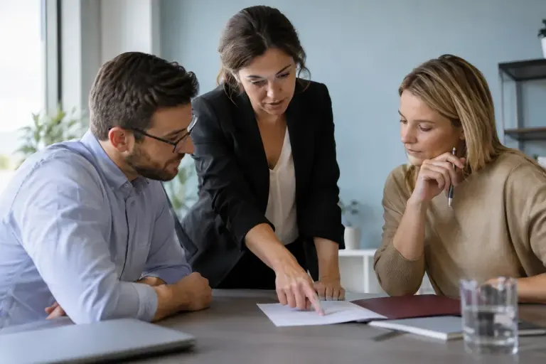 Three colleagues reviewing a decision note with a burgundy folder on the table.