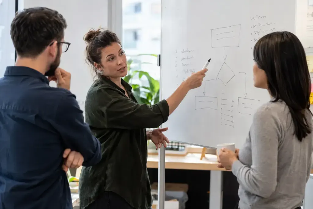 Three colleagues discussing a small decision diagram on a whiteboard with indistinct writing.